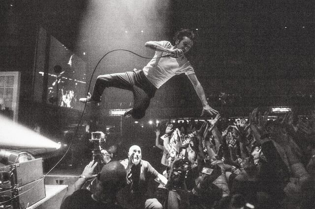 Zwart-witfoto van een crowdsurfer boven een uitgestrekte concertmenigte