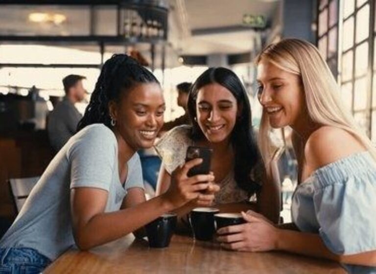 Drie vrouwen praten en lachen samen aan een tafel in een café