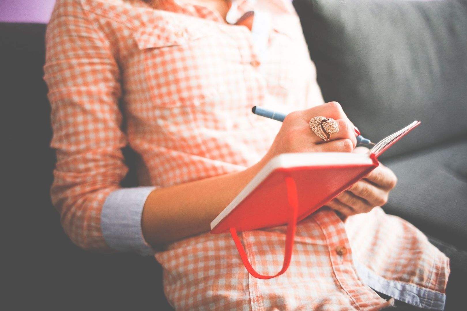 Persoon schrijft met een pen in een rood notitieboek op schoot